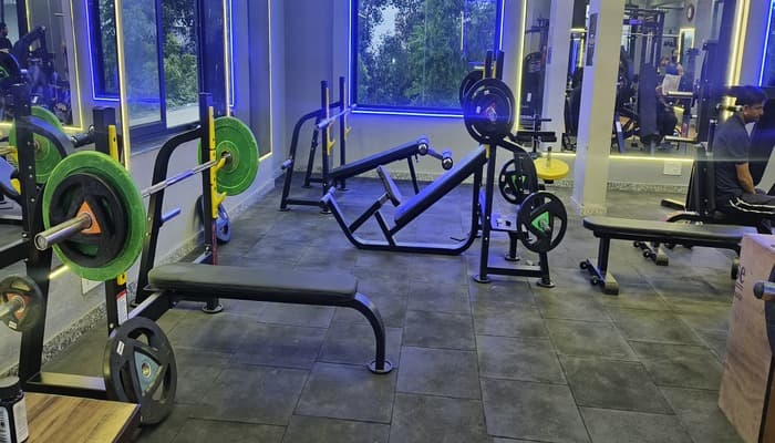 Free-weight area with barbells and benches under blue lighting at G2 Fitness Club