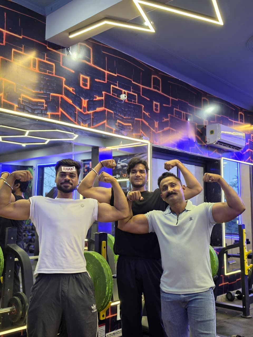 Three members flexing their biceps together on the G2 Fitness Club training floor